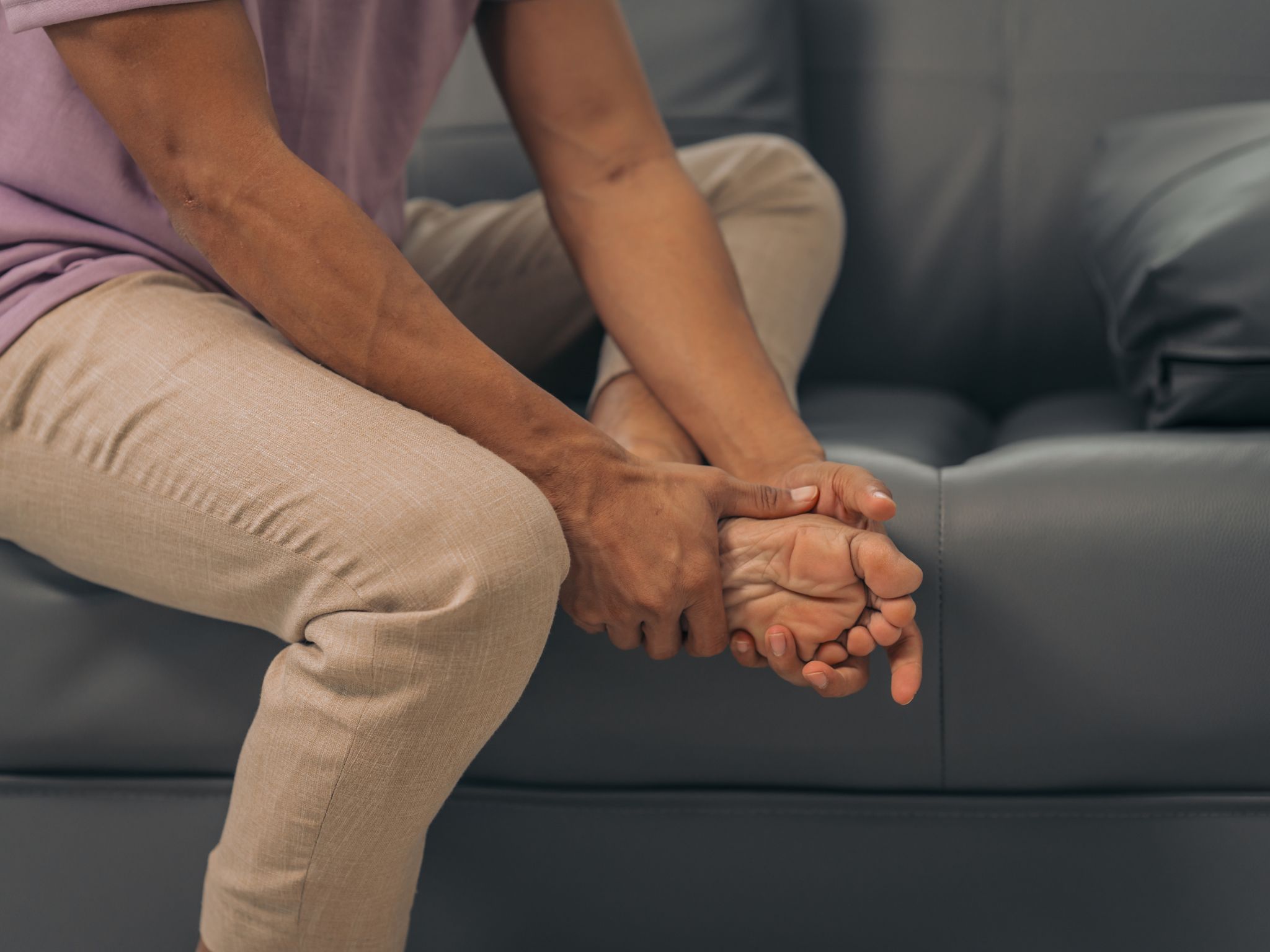 Middle-aged Asian Indian man with ankle disease, plantar pain, sitting on the sofa.